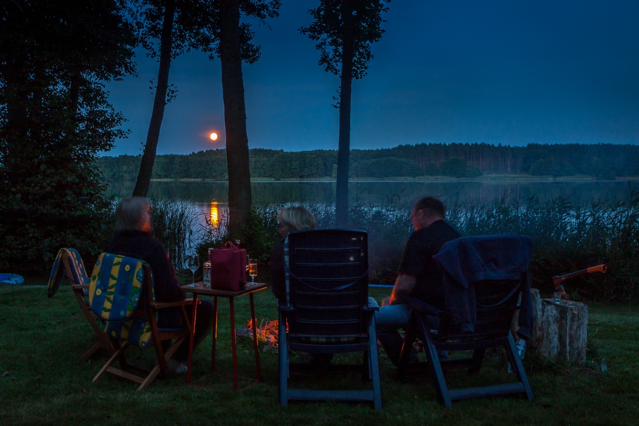 Gruppe am Lagerfeuer am Ufer des Rudower Sees in der Prignitz, im Hintergrund der aufgehende Mond